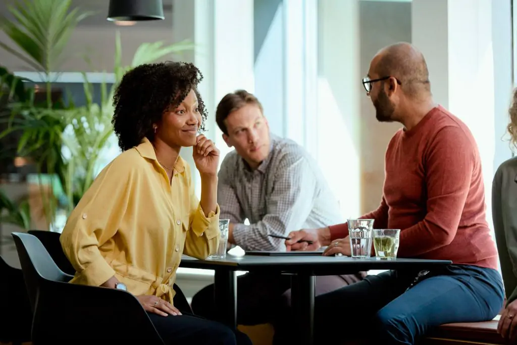 Drei Personen sitzen an einem Tisch im Büro und sprechen miteinander